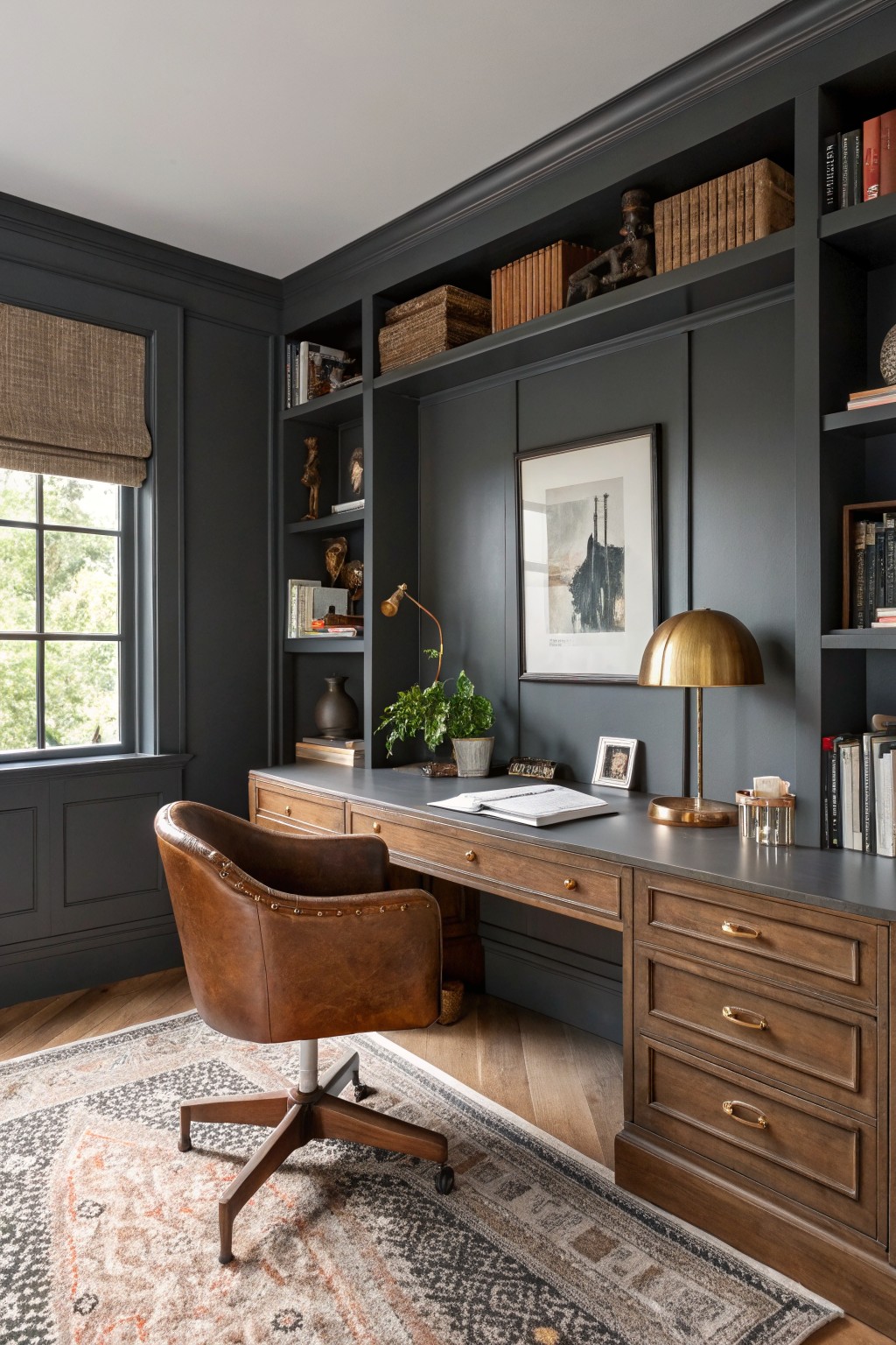 Cozy home office featuring deep charcoal gray walls with built-in wood shelving, a leather desk chair, brass lamps, and bookshelves filled with vintage volumes