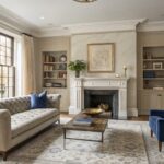 Elegant living room featuring pale greige walls, cream sofa, navy blue velvet chair, marble fireplace, and large windows with natural light