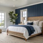 Bedroom featuring deep navy shiplap accent walls, white beamed ceiling, wooden bed with white linens and blue throw, rattan benches, and large windows with sheer curtains