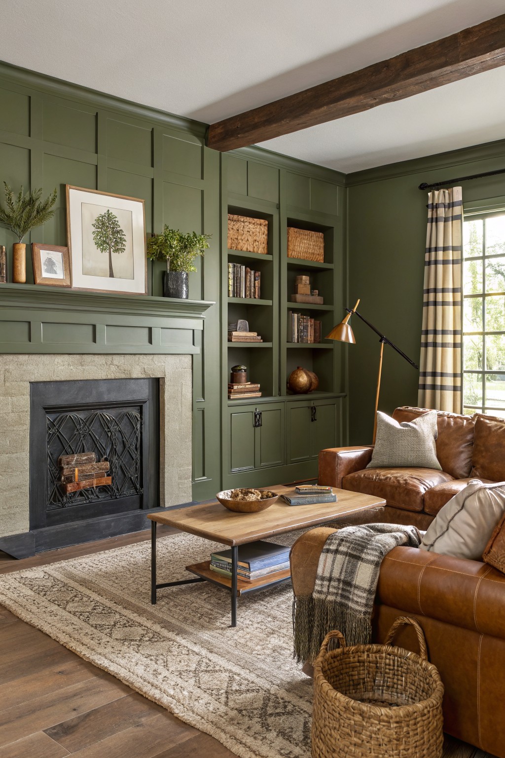 Cozy reading room with sage green paneled walls, black stone fireplace, brown leather sofa, wood coffee table, and woven rug
