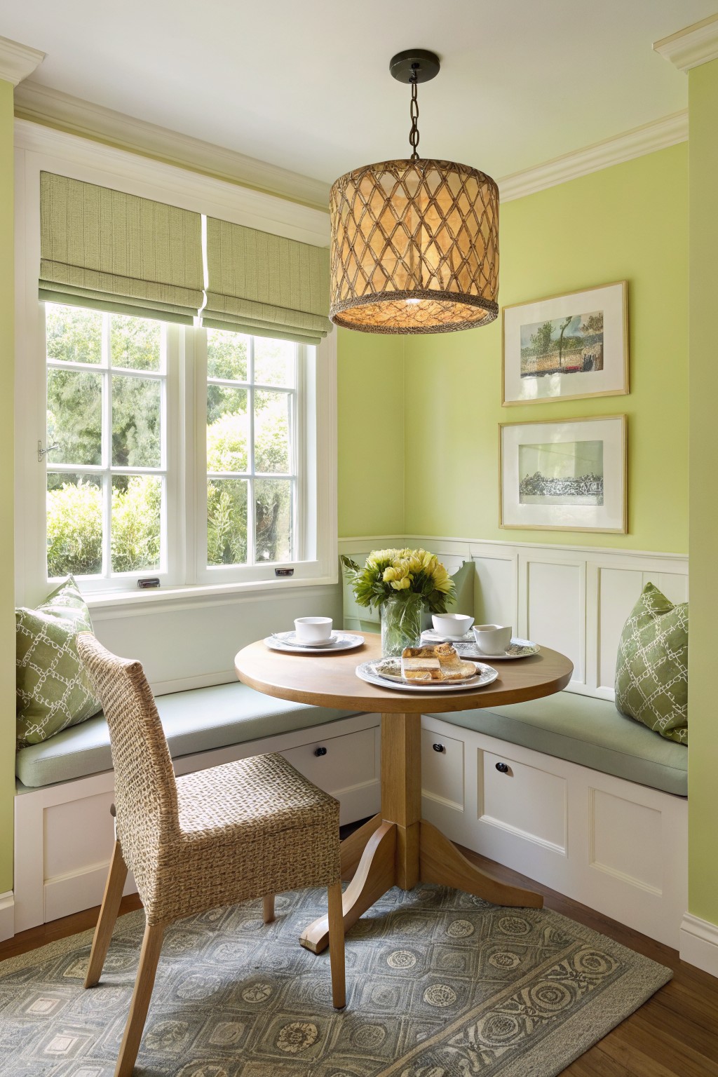 Breakfast nook with pale sage green walls, white wainscoting, round wood table, green cushions, and rattan pendant light