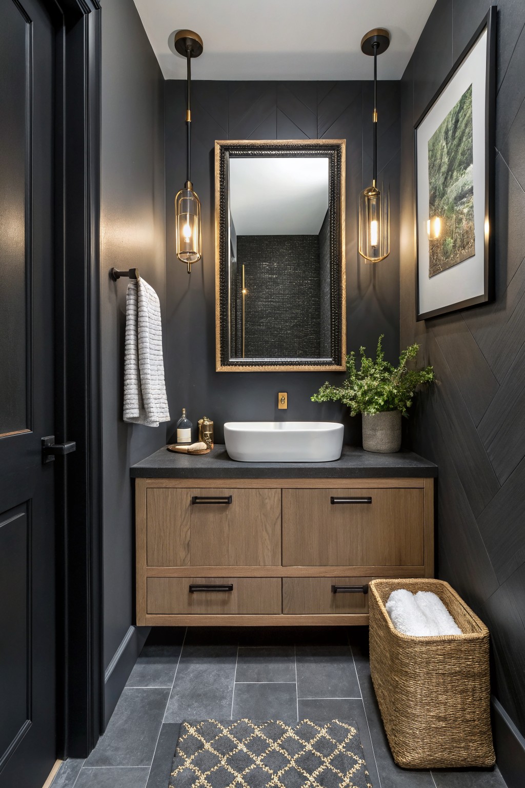 Small modern powder room with dark charcoal gray walls, wood vanity, white vessel sink, gold pendant lights, framed art, plants, and black door.