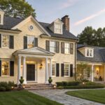 A two-story house with soft yellow siding and white trim around the front entrance.