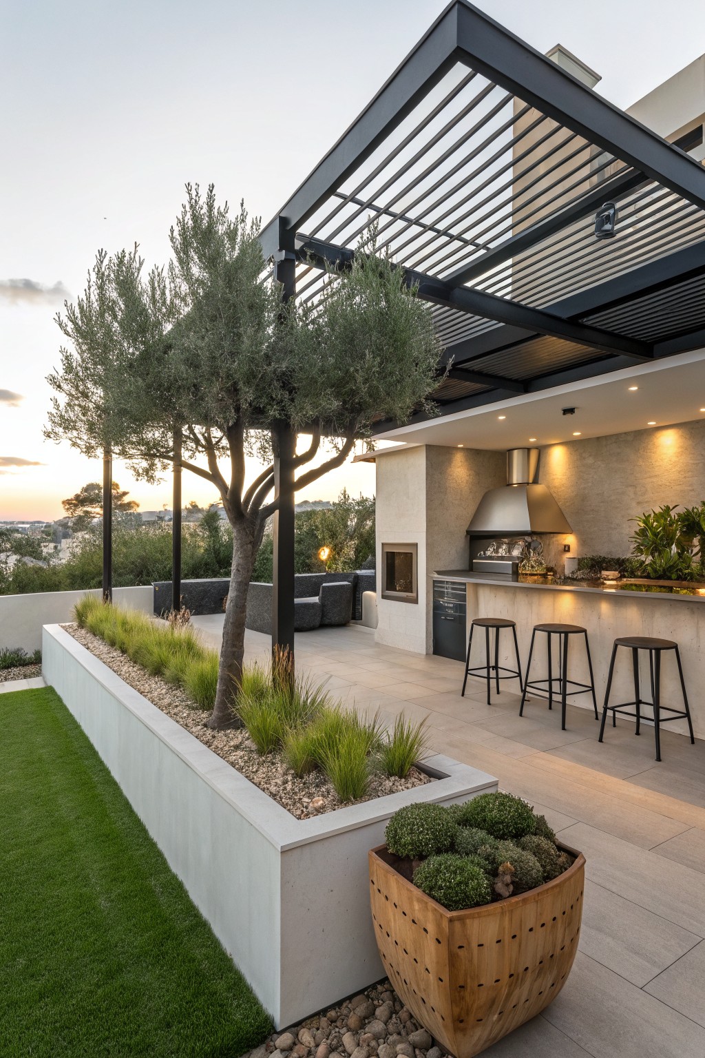 Outdoor kitchen bar with built-in grill and stools under black slatted metal pergola on tiled patio, featuring olive tree, raised planters with grasses, lounge seating, and stone walls at dusk.