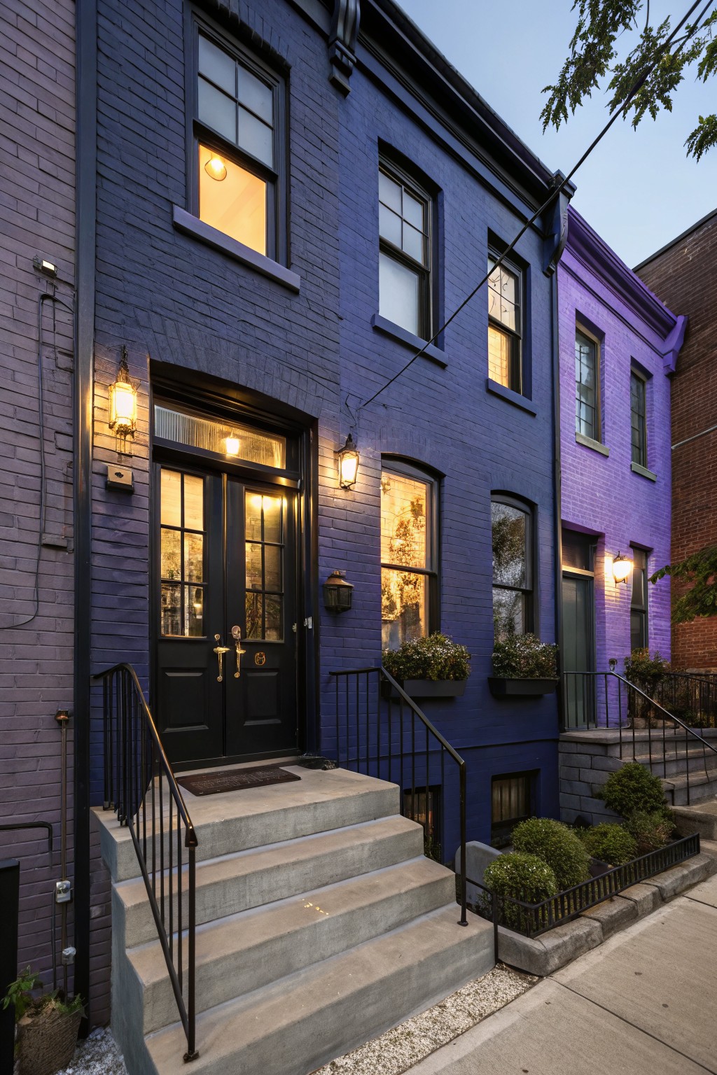 A two-story brick row house painted in deep navy blue with concrete front steps and black door trim.