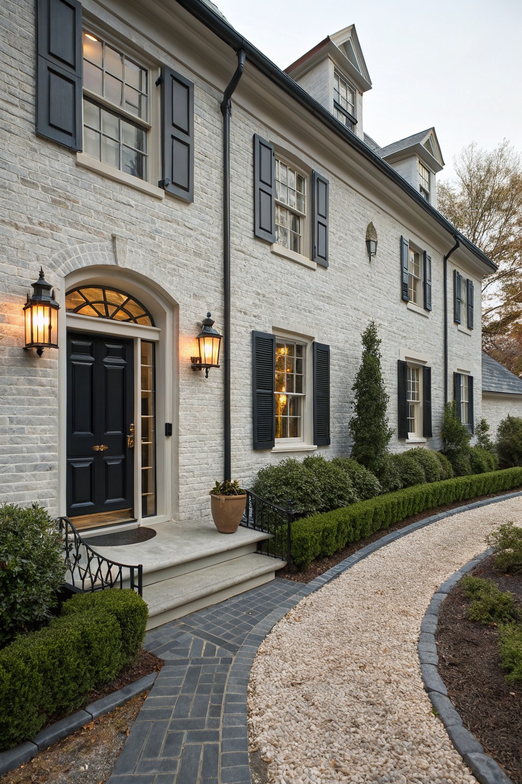 A two-story brick house painted in a soft white with dark shutters and trim.