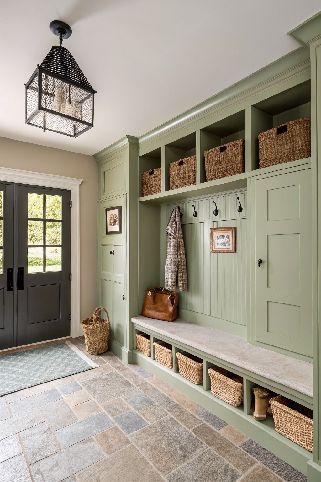 Built-in sage green cabinetry and bench in a stone-tiled entryway.