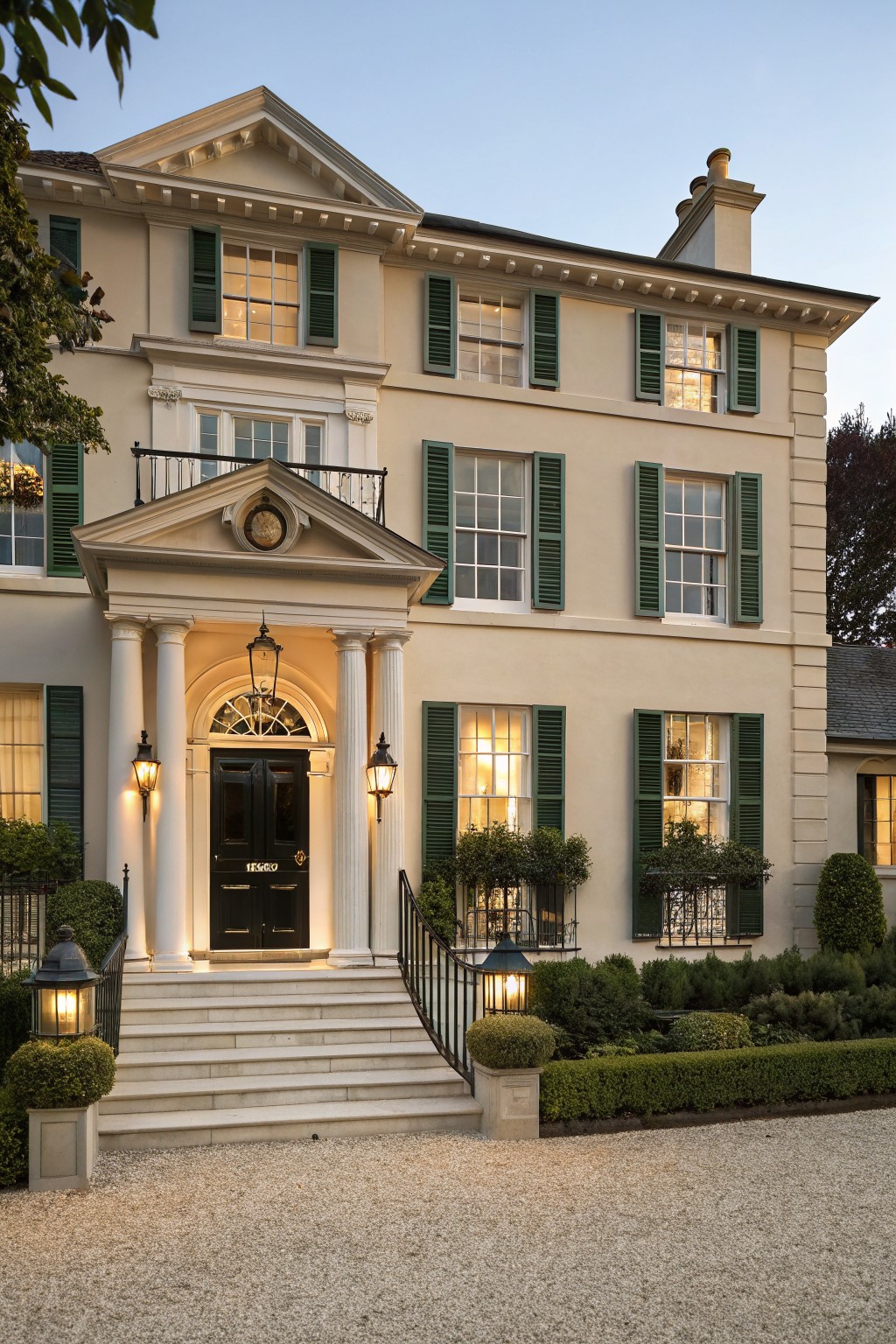 A large two-story house painted in soft warm beige with green shutters and white trim.