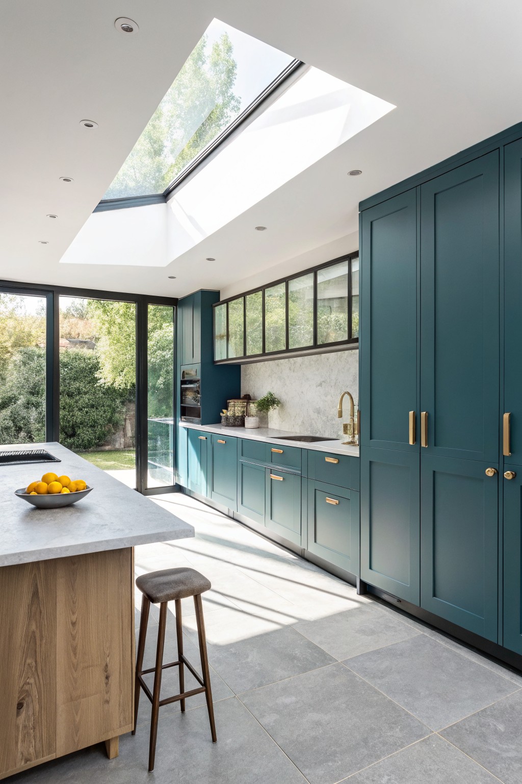 Modern kitchen with blue cabinetry, marble accents, skylight, and a wooden bar stool.