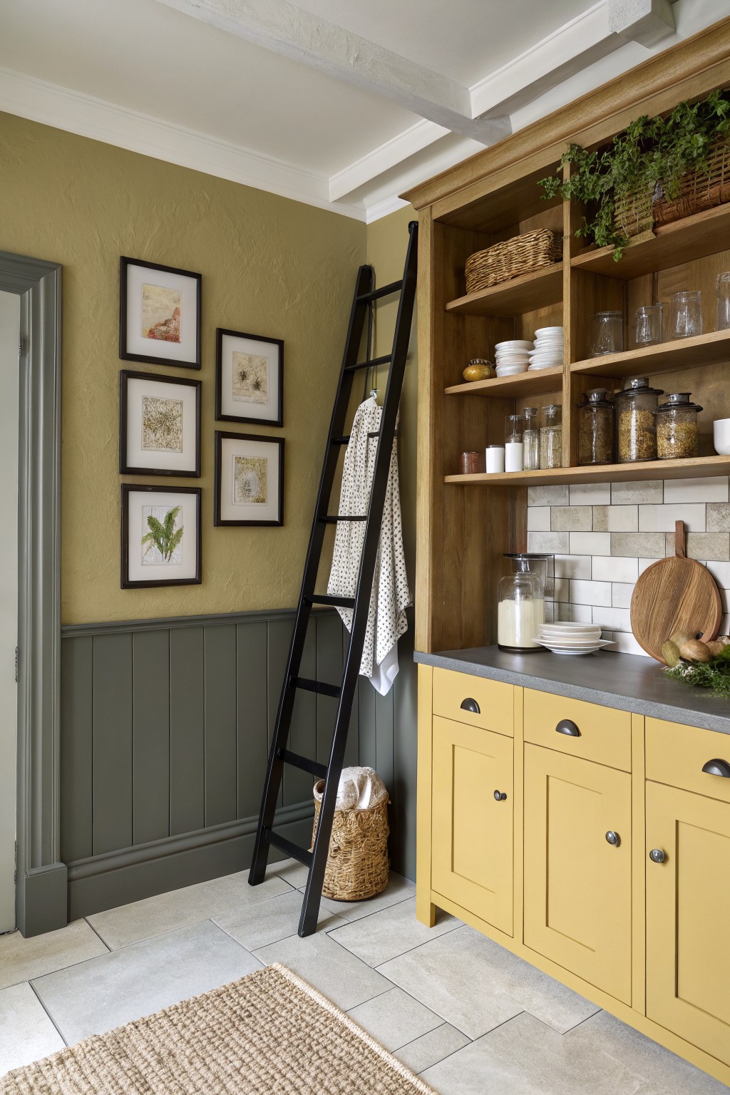 Olive green walls above gray wainscoting in a room with wooden open shelving and yellow cabinets.