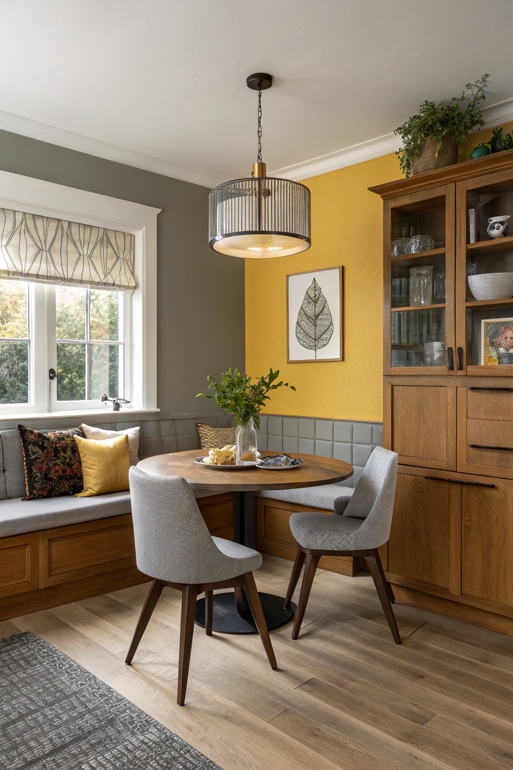 A mustard yellow accent wall in a dining area with wood cabinetry and gray wainscoting.
