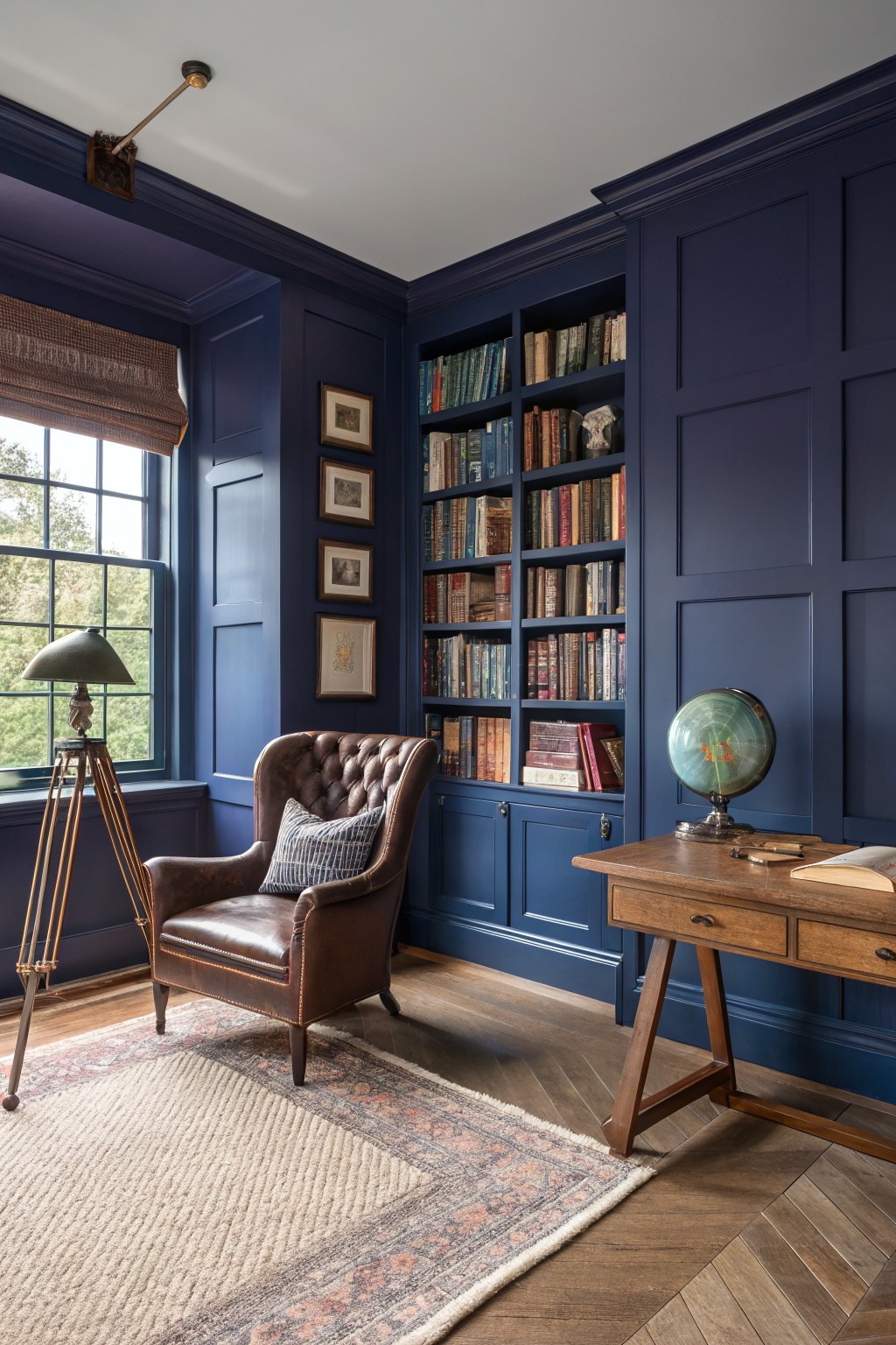 Cozy blue-hued study with a leather armchair, bookshelves, globe, and wooden desk.