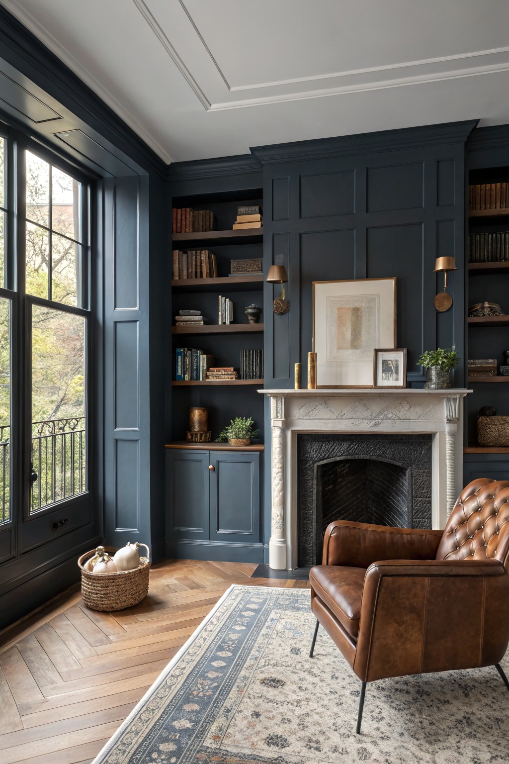 A sitting room with deep navy blue built-in bookshelves and paneling surrounding a marble fireplace.