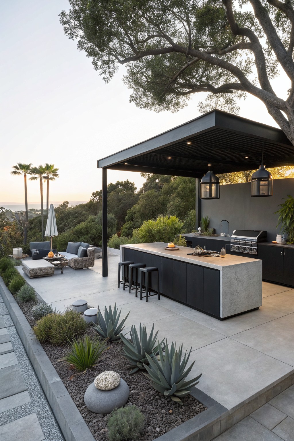 A modern outdoor kitchen featuring a large concrete island with bar stools, a built-in grill, and dark cabinetry under a covered structure on a landscaped patio.