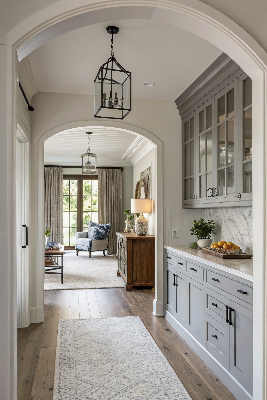 Light gray cabinets in a farmhouse kitchen with wood floors and an arched opening.