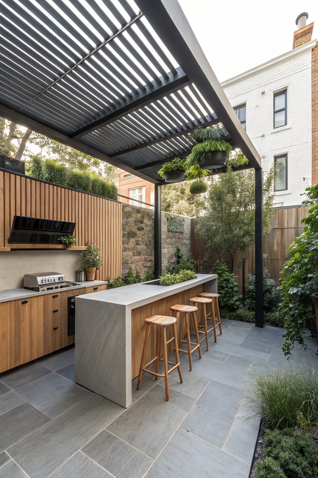 Modern outdoor kitchen with concrete island, wooden stools, and slatted pergola overhead.