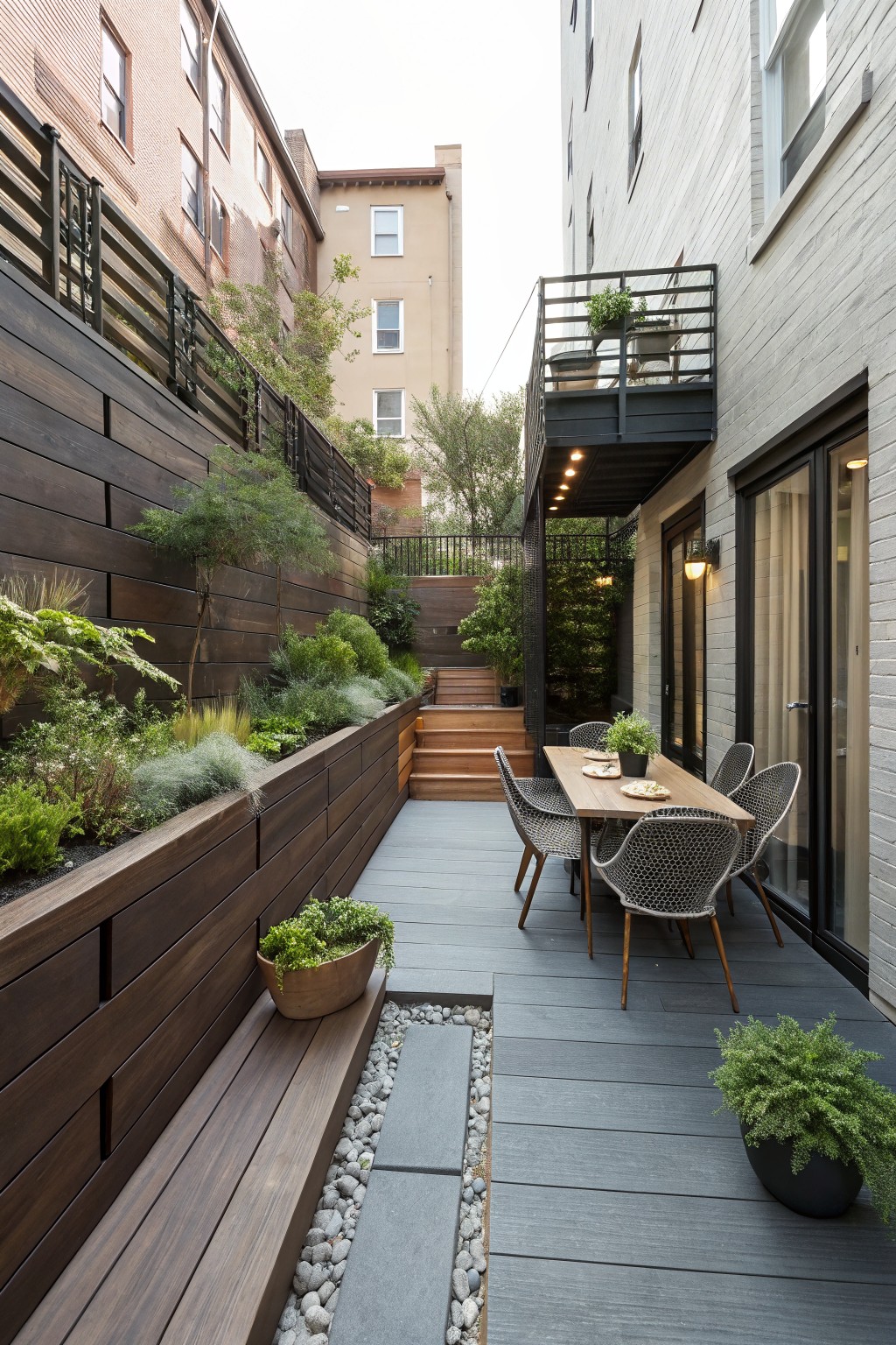 Modern urban patio with dining table, woven chairs, decking, and lush garden wall.