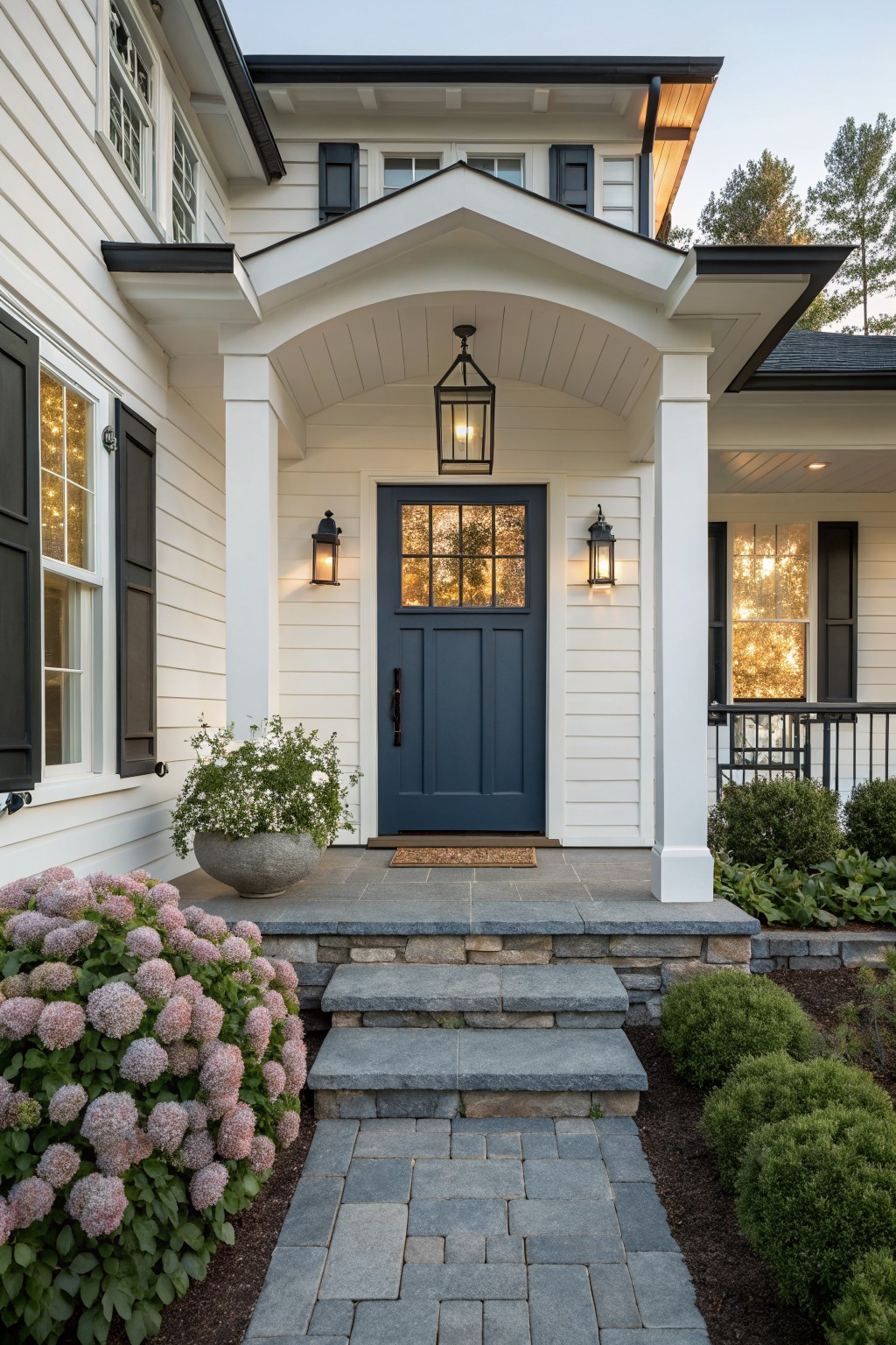 White house with navy door, stone steps, lantern lights, and pink hydrangeas.