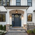 White house with navy door, stone steps, lantern lights, and pink hydrangeas.