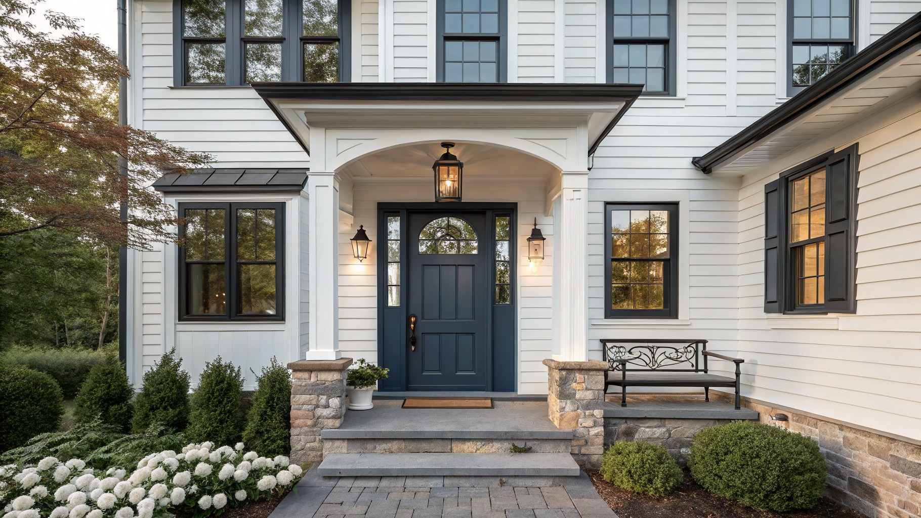 White house with navy door, stone steps, lantern lights, and pink hydrangeas.