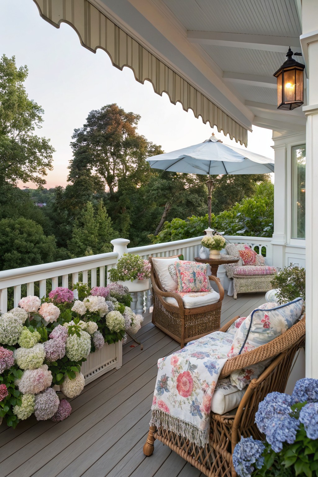 A wooden deck porch with wicker seating, a large light blue umbrella, striped awning overhead, and many planters of hydrangeas along the white railing.