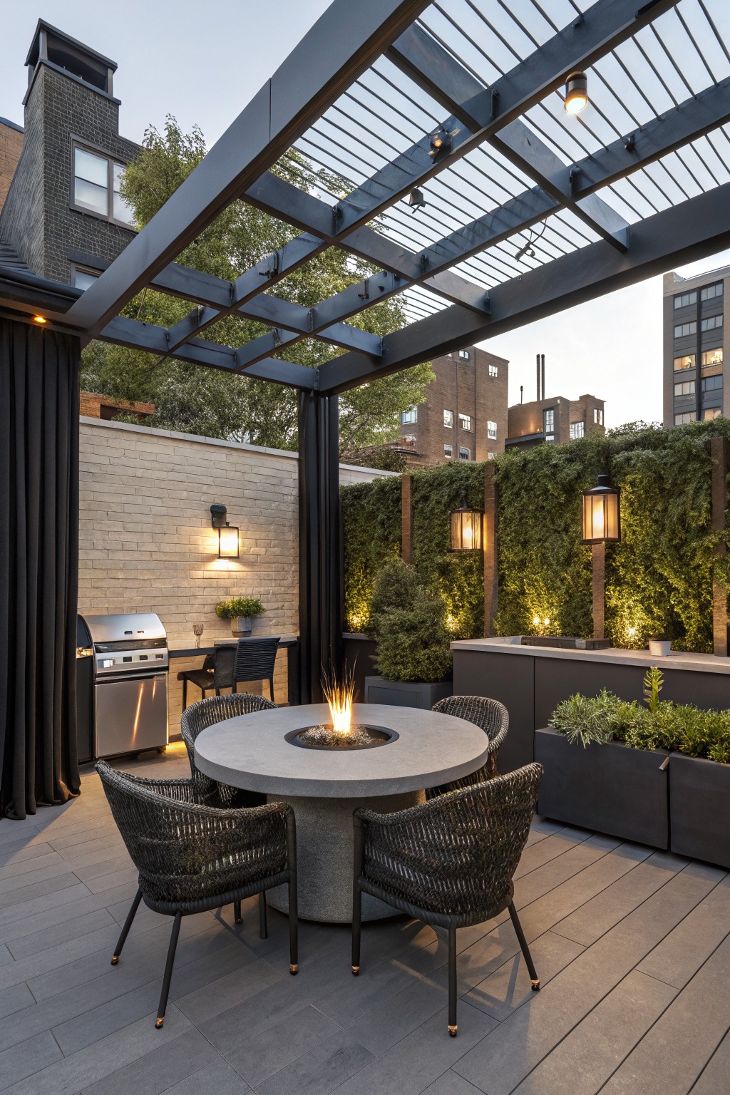An outdoor patio under a dark metal pergola featuring a round concrete fire pit table with woven chairs, black side curtains, and vertical green walls in the background.