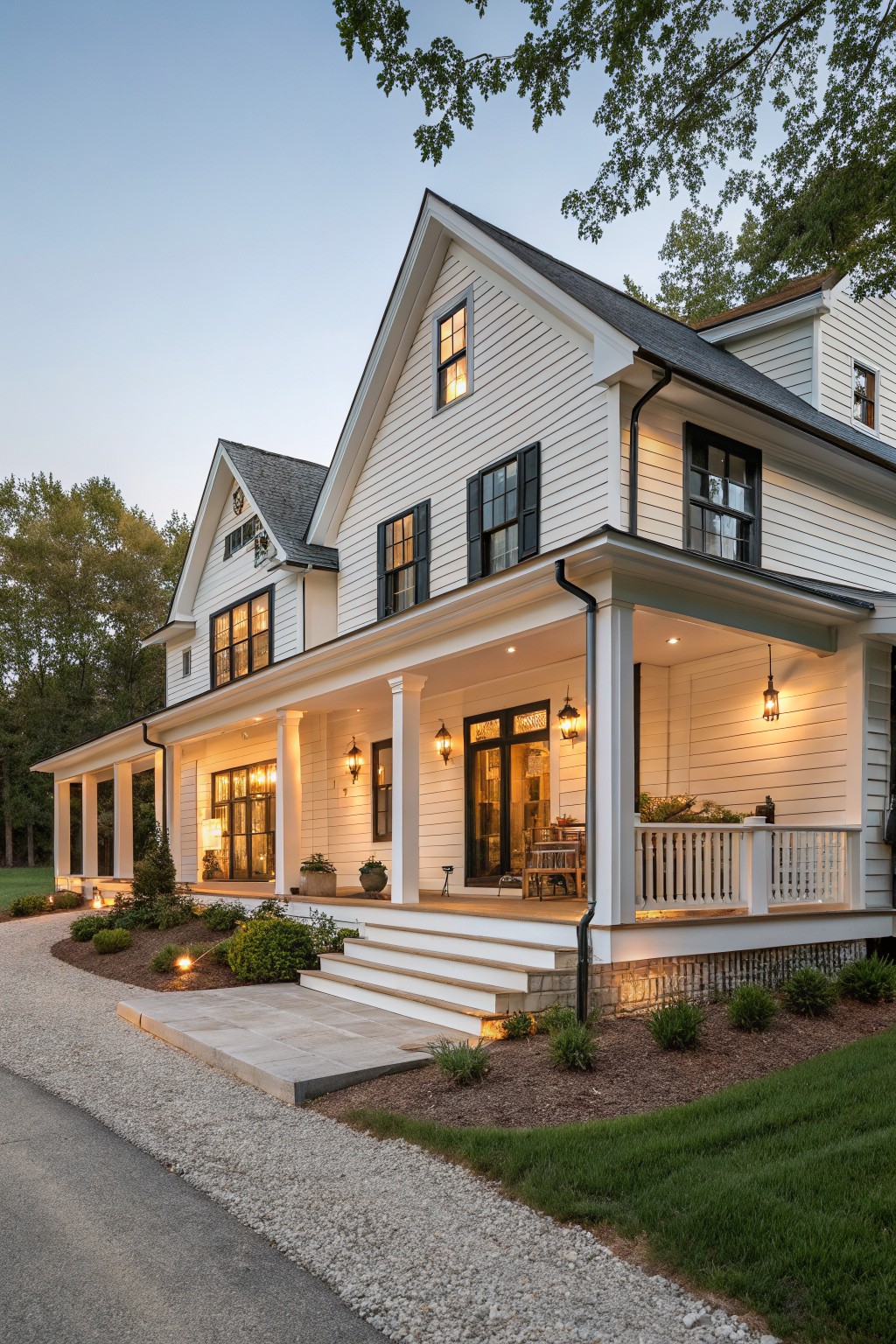 White two-story house with black shutters, lit porch, and landscaped steps at dusk.