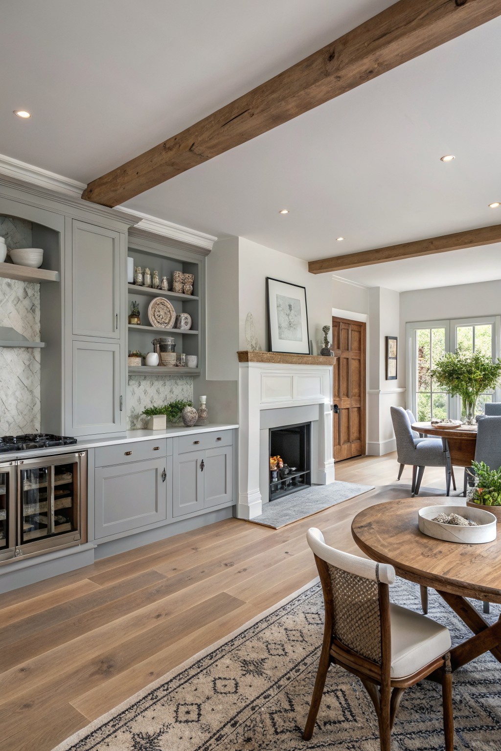 Light gray cabinets in an open farmhouse kitchen with wood floors and a fireplace.