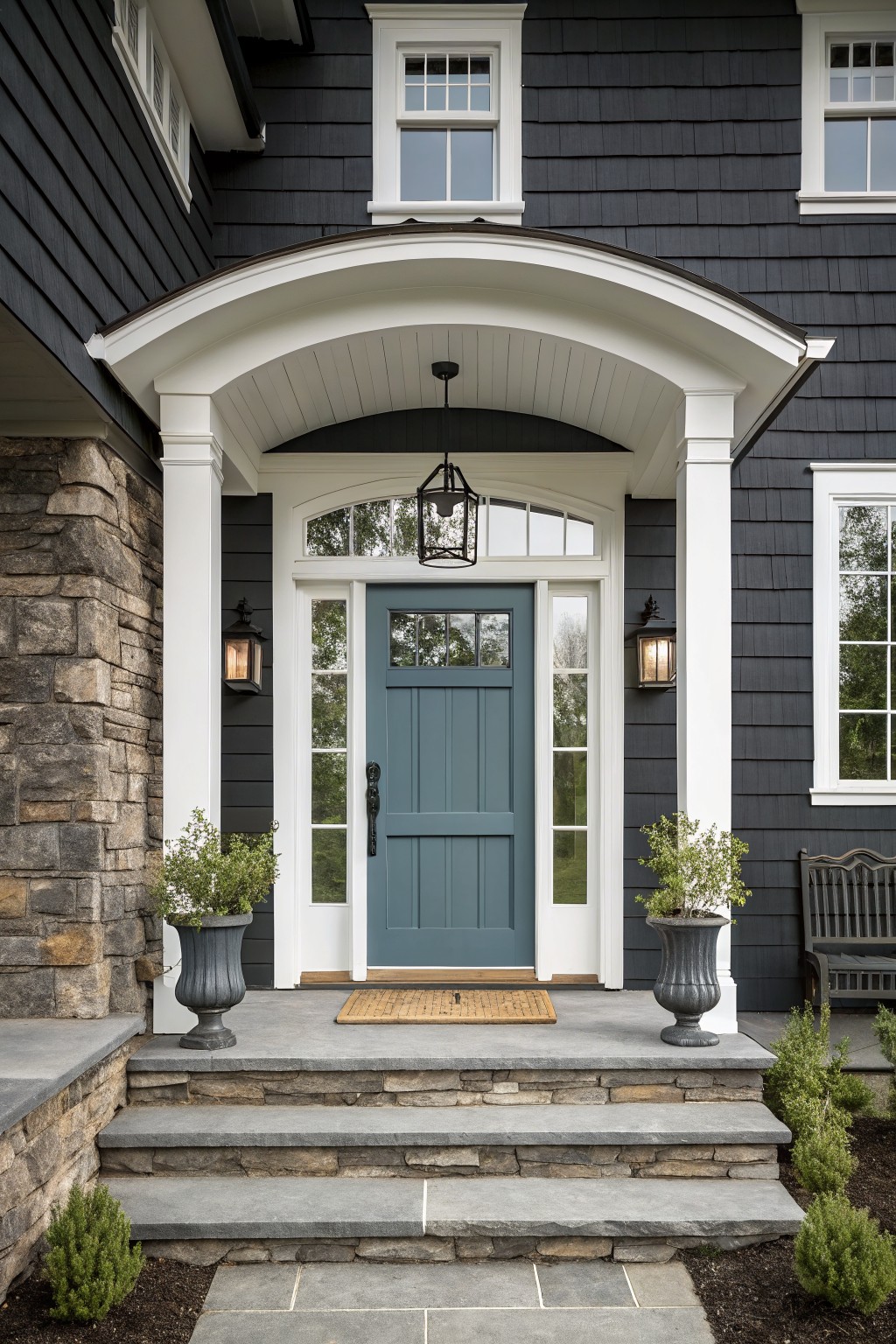 A muted blue front door with white trim on a dark shingled house.