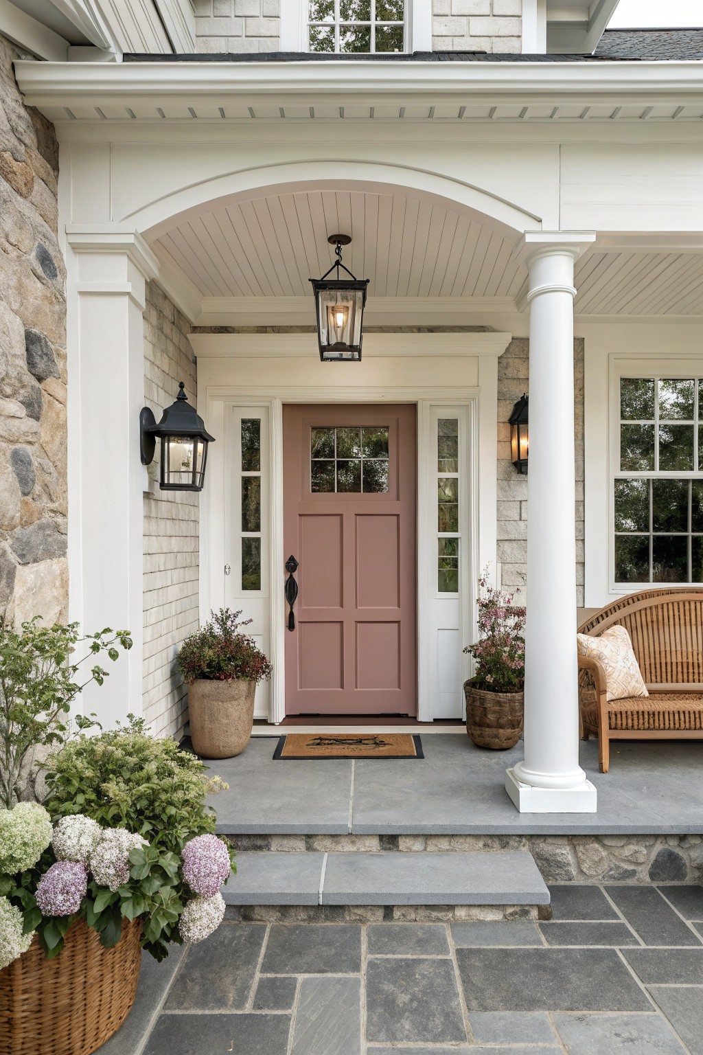 A muted dusty rose front door on a white-trimmed farmhouse porch.
