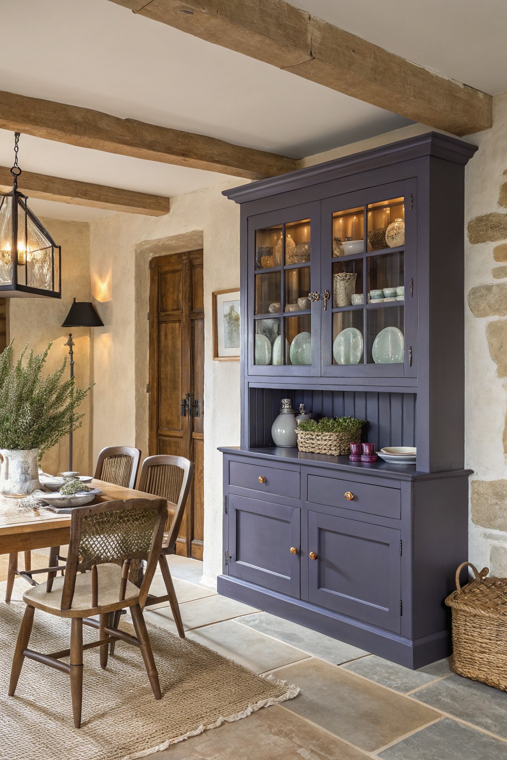 A dark moody blue painted hutch in a rustic dining room with wood beams and stone walls.