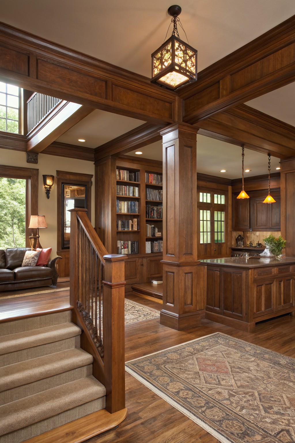 Luxurious wood-paneled interior with staircase, bookshelves, leather sofa, and kitchen island