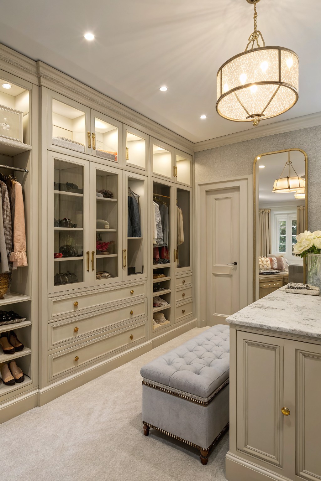 Light greige built-in cabinetry in a walk-in closet with carpet and a tufted bench.