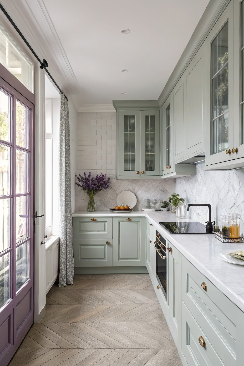 A kitchen with soft sage green cabinets, white tile, and marble counters.