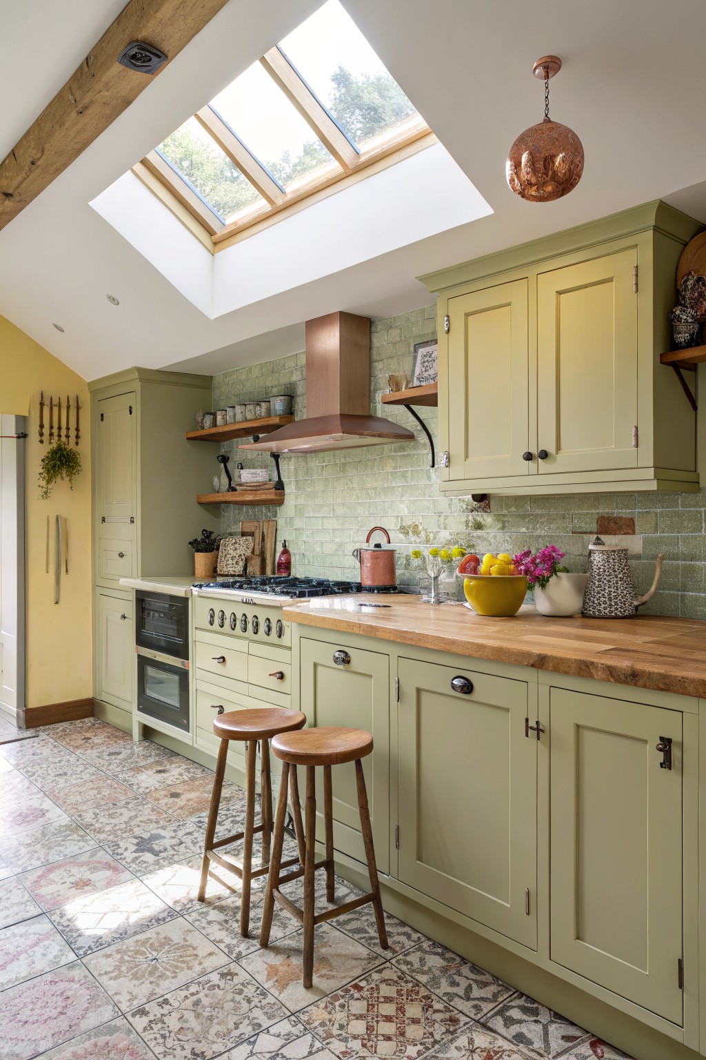 Sage green kitchen cabinets with wood countertops under a skylight.