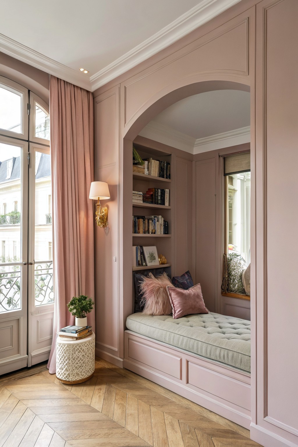 Pink arched alcove with built-in tufted daybed, bookshelves, and French doors