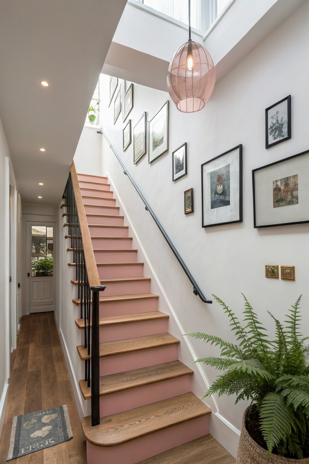Pink staircase with wooden treads, black railing, framed art, and pendant light.