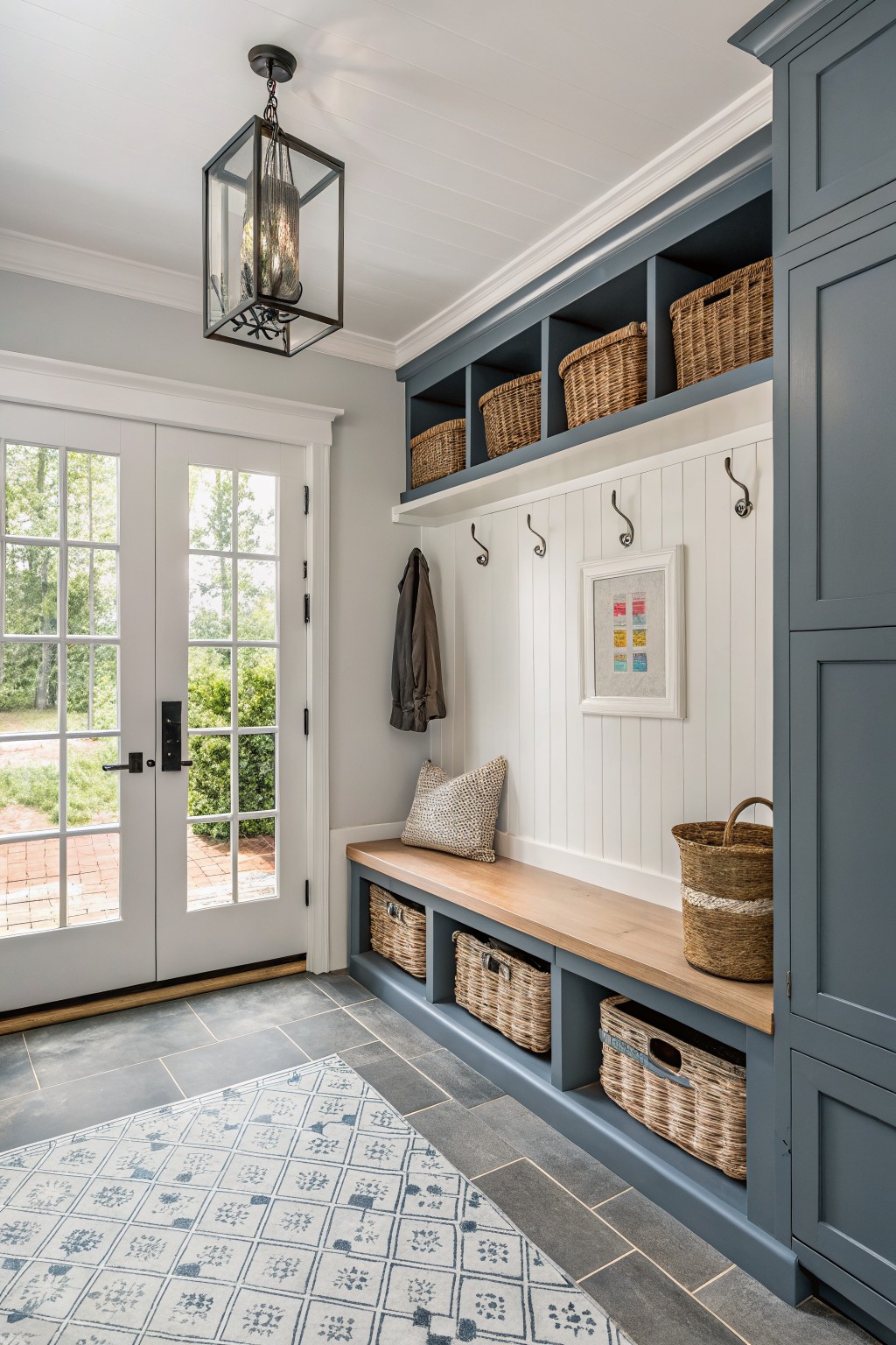 Blue mudroom with wooden bench, woven baskets, hooks, lantern, and double doors