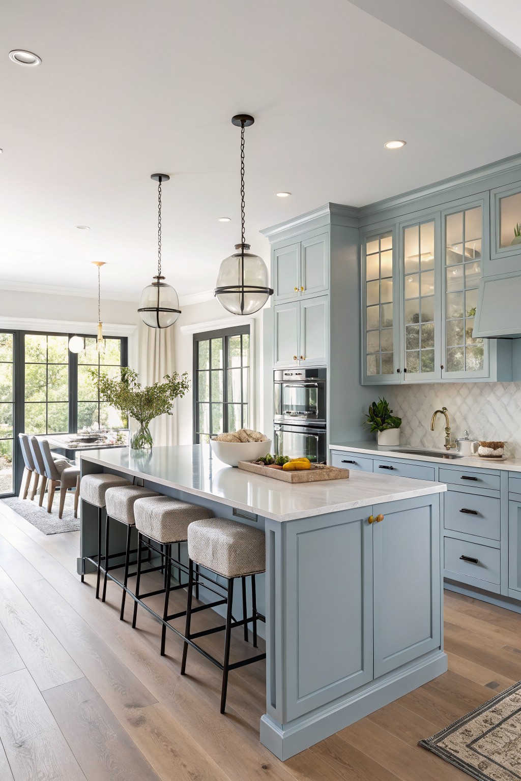 Soft blue gray kitchen cabinets with a white marble island and wood flooring.
