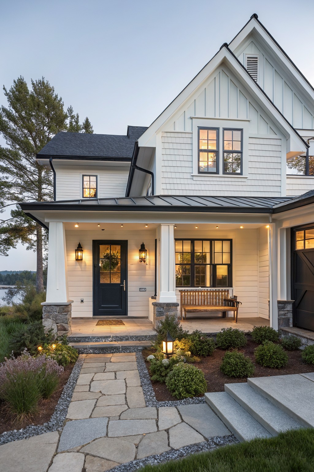 White two-story house with black door, lit porch bench, and stone garden path at dusk