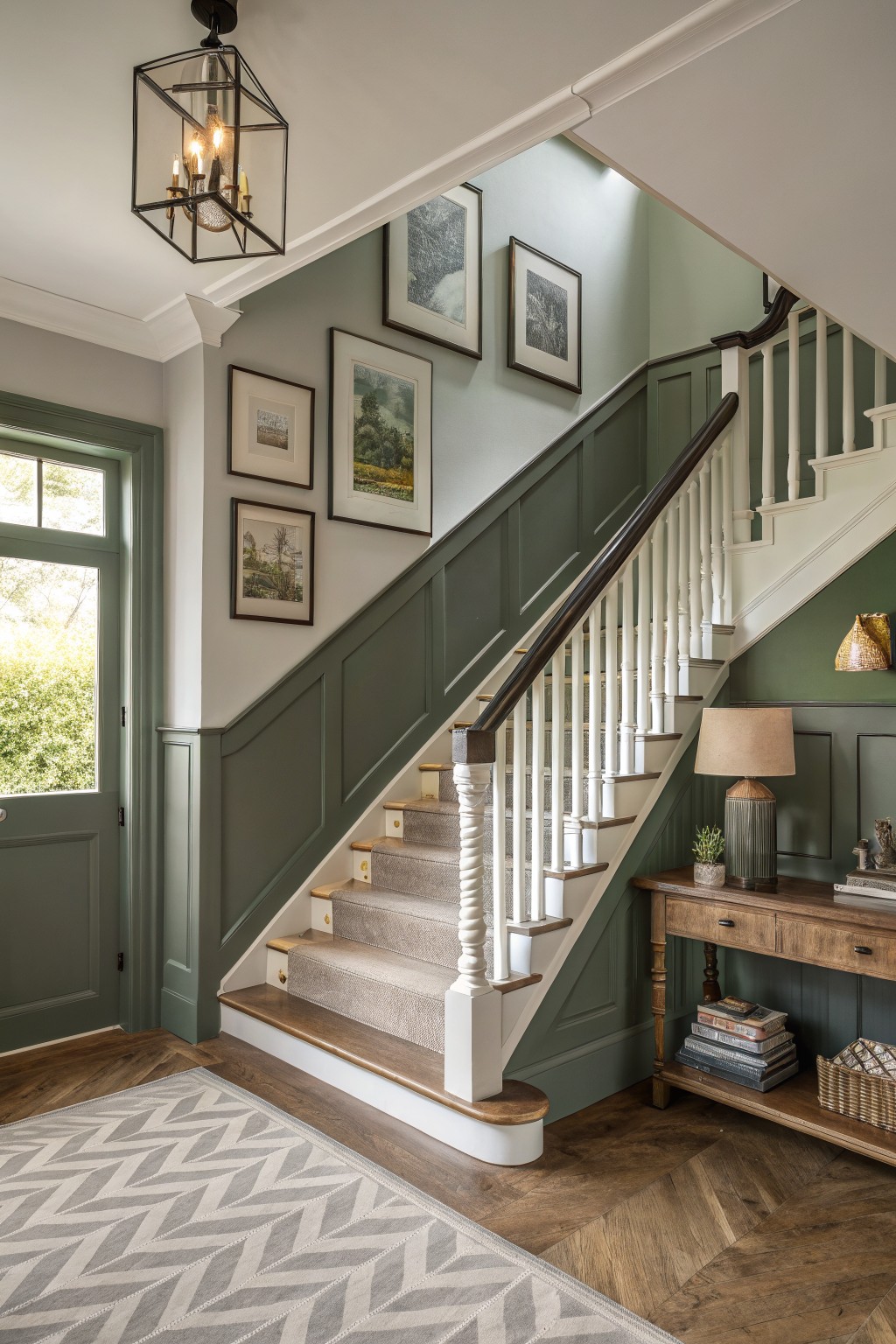 A staircase features muted sage green paneling with white railings and wood treads.