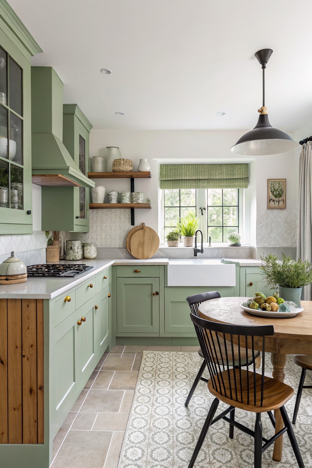 Sage green kitchen cabinets with a white sink and wood table in the foreground.