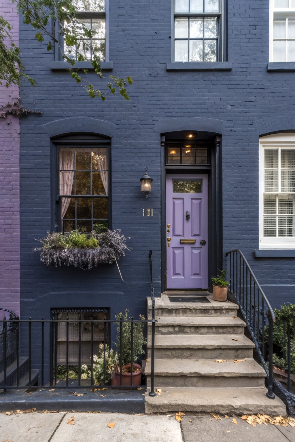 A brick row house painted deep navy with concrete steps and black railings.