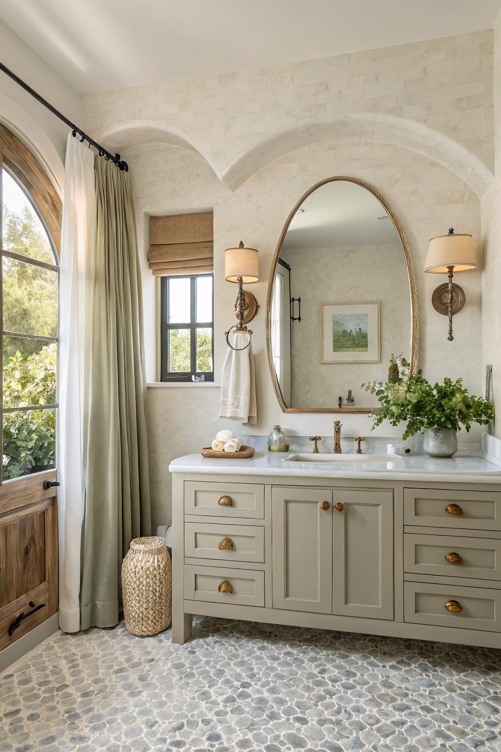 Elegant bathroom with arched mirror, gray vanity, marble sink, and pebble floor.