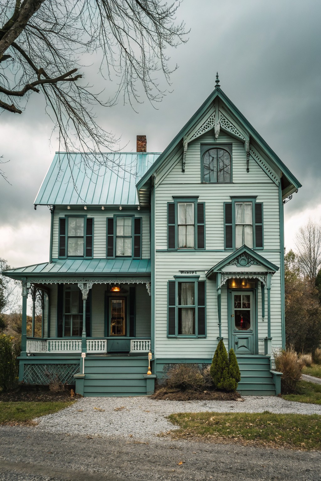 Victorian house with pale blue siding, teal roof, porch, and gravel driveway under clouds