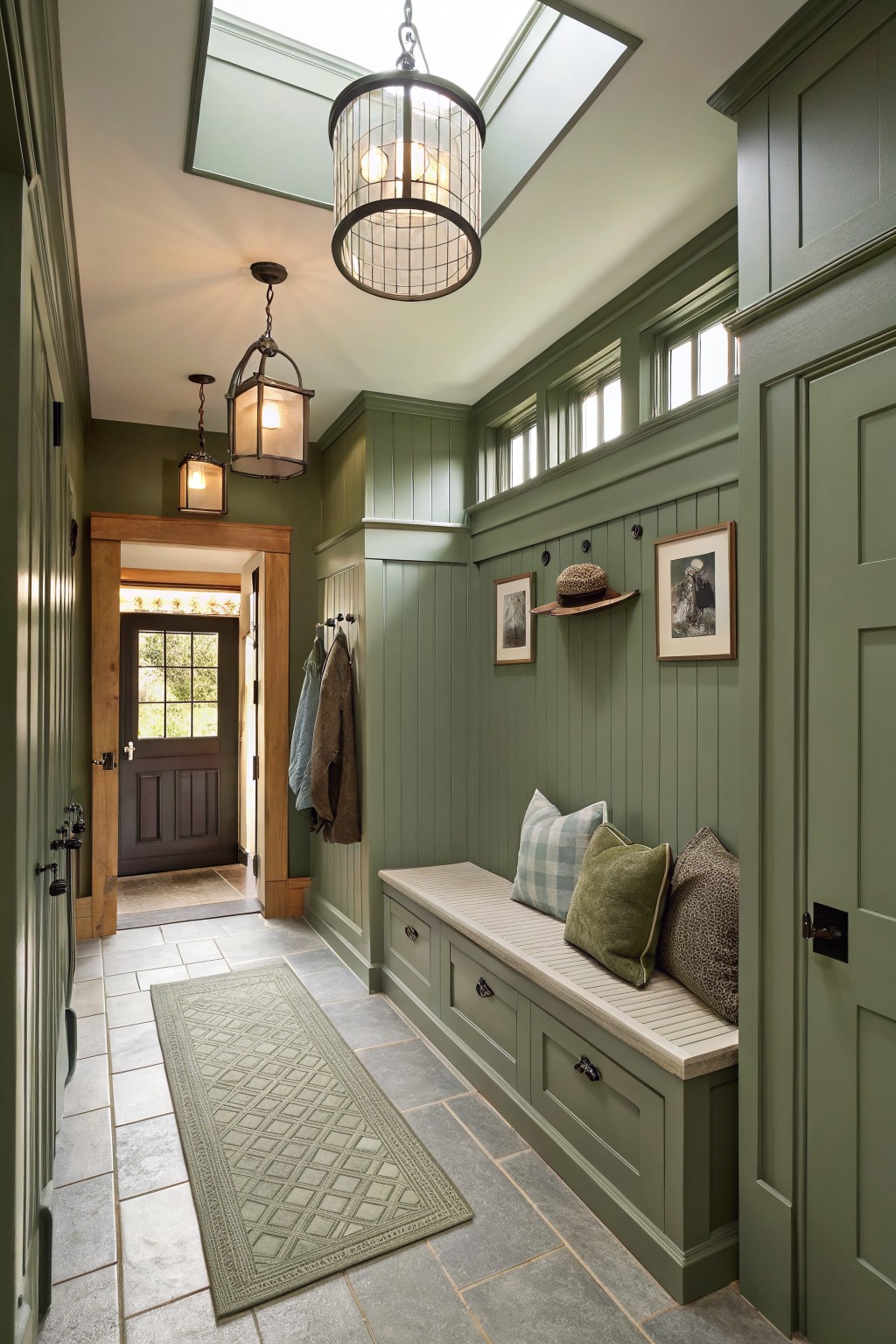 Green mudroom with storage bench, skylights, lanterns, coats, and patterned rug