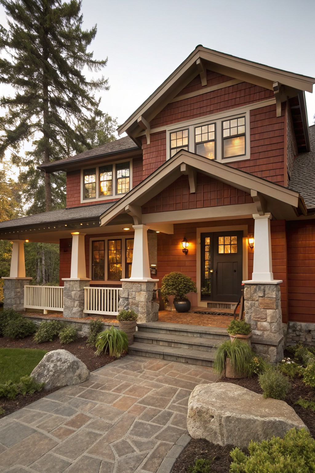Red shingled house with stone pillars, porch, steps, and landscaped stone path at dusk.
