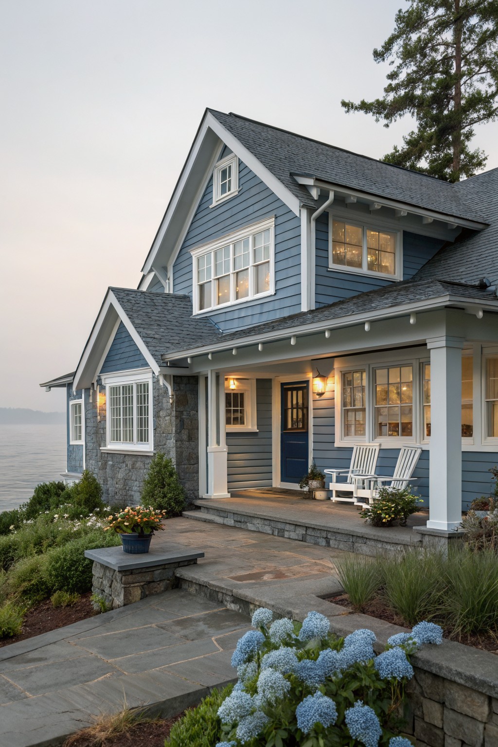 Blue coastal house with white trim, porch chairs, and hydrangeas by the water