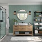 A bathroom with soft sage green walls, a round mirror, and a light wood vanity.