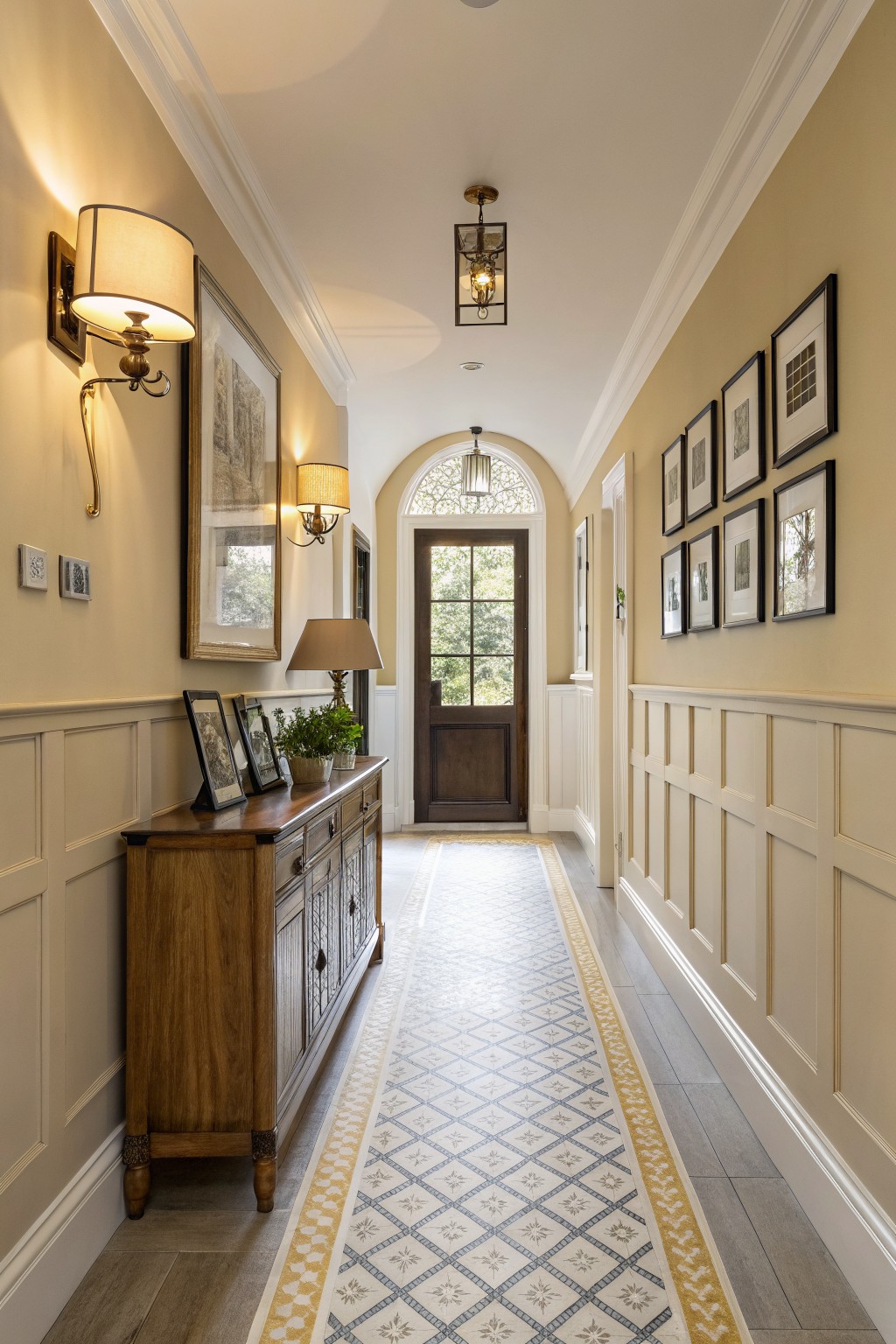 A hallway with warm beige walls above white wainscoting and a wood console table.